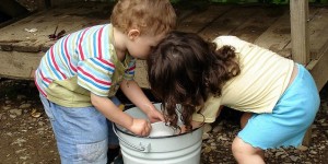 Two children, a boy and a girl, wash dishes in a bucket.