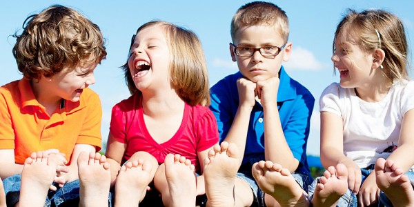 Four kids sit in a row; three are laughing, one seems unhappy and left out