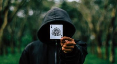 man in a hood holding up a playing card